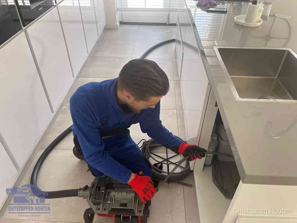 Een monteur ontstopt de keukenafvoer onder de spoelbak met een elektrische veermachine in Houten