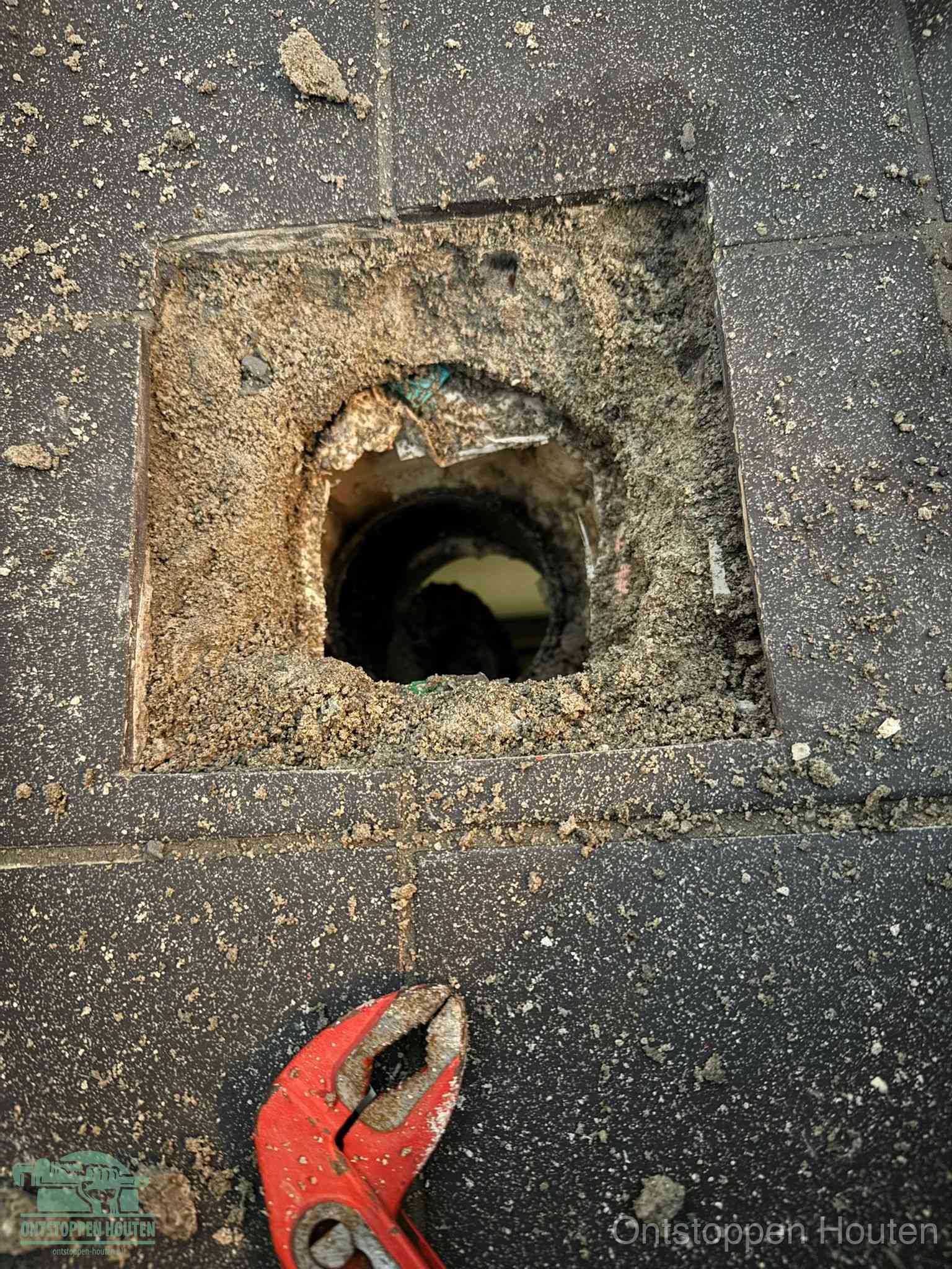 Een geopend rioolputje in een betontegelvloer met losgemaakt rooster en een zichtbare ronde afvoerbuis, het achterhalen waar de afvoerverstopping zit in Houten