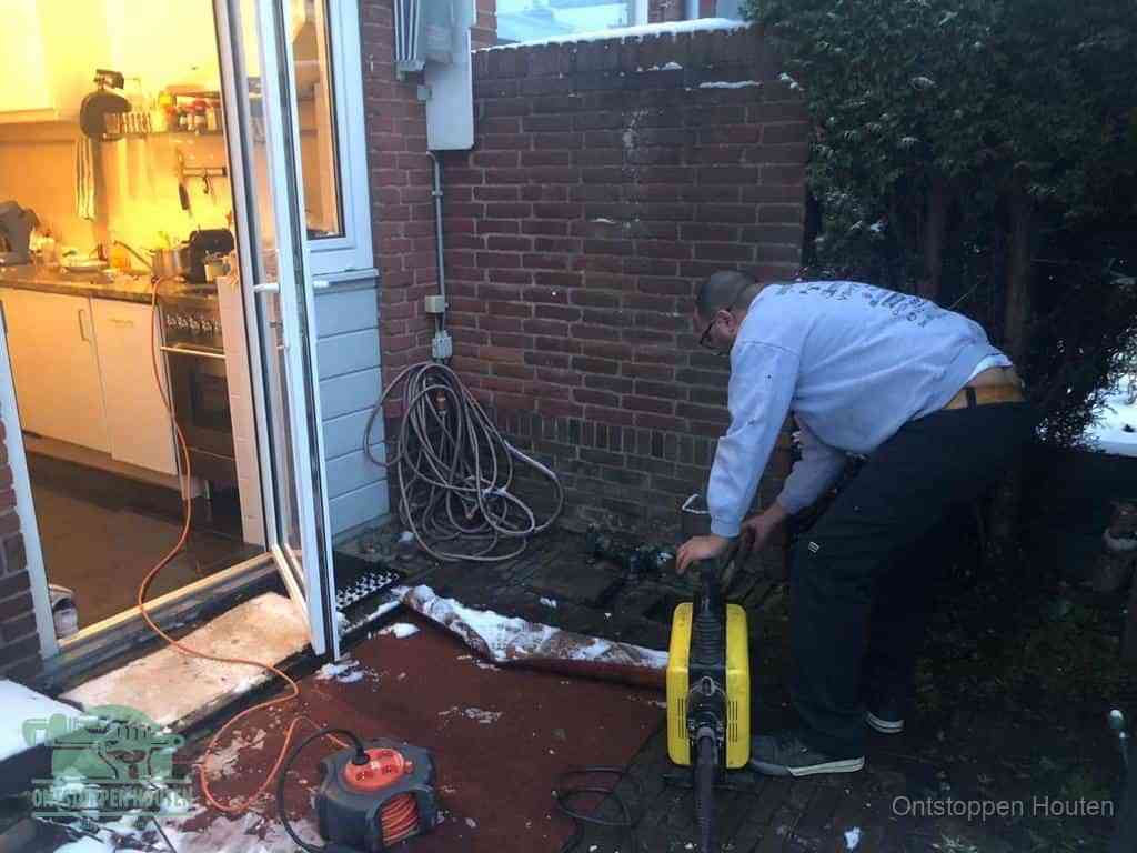 Een monteur werkt buiten bij een open riool-/grondput met een elektrische ontstoppingsmachine om een verborgen afvoerprobleem op te sporen in Houten