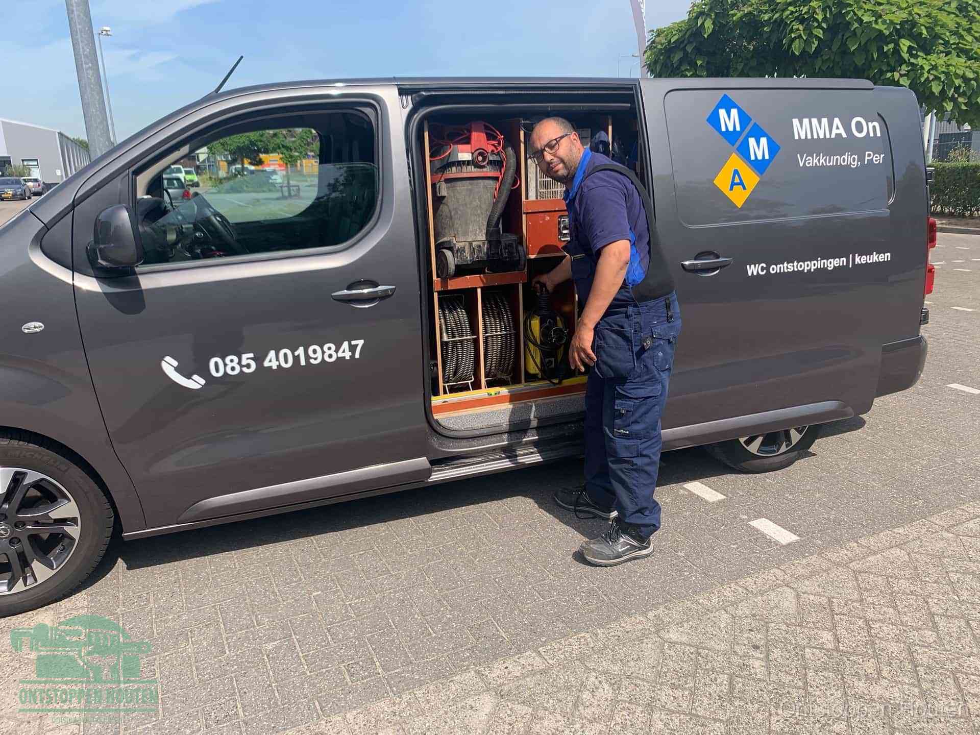 Een monteur bij de open schuifdeur van zijn bedrijfsbus op een parkeerplaats, klaar om de oorzaak van terugkerende afvoerverstoppingen aan te pakken in Houten