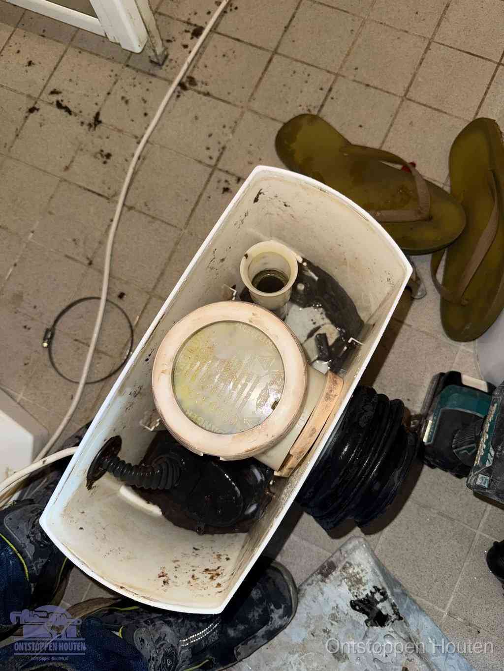Een gedemonteerde toiletpot op de vloer met ontstoppingsveer en gereedschap ernaast, het verwijderen van een vastzittend voorwerp uit de wc in Houten