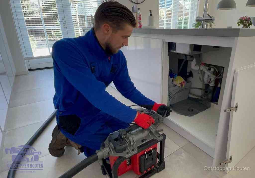 Een monteur voert een professionele elektrische ontstoppingsmachine in de afvoer onder de spoelbak tijdens het gootsteen ontstoppen in Houten